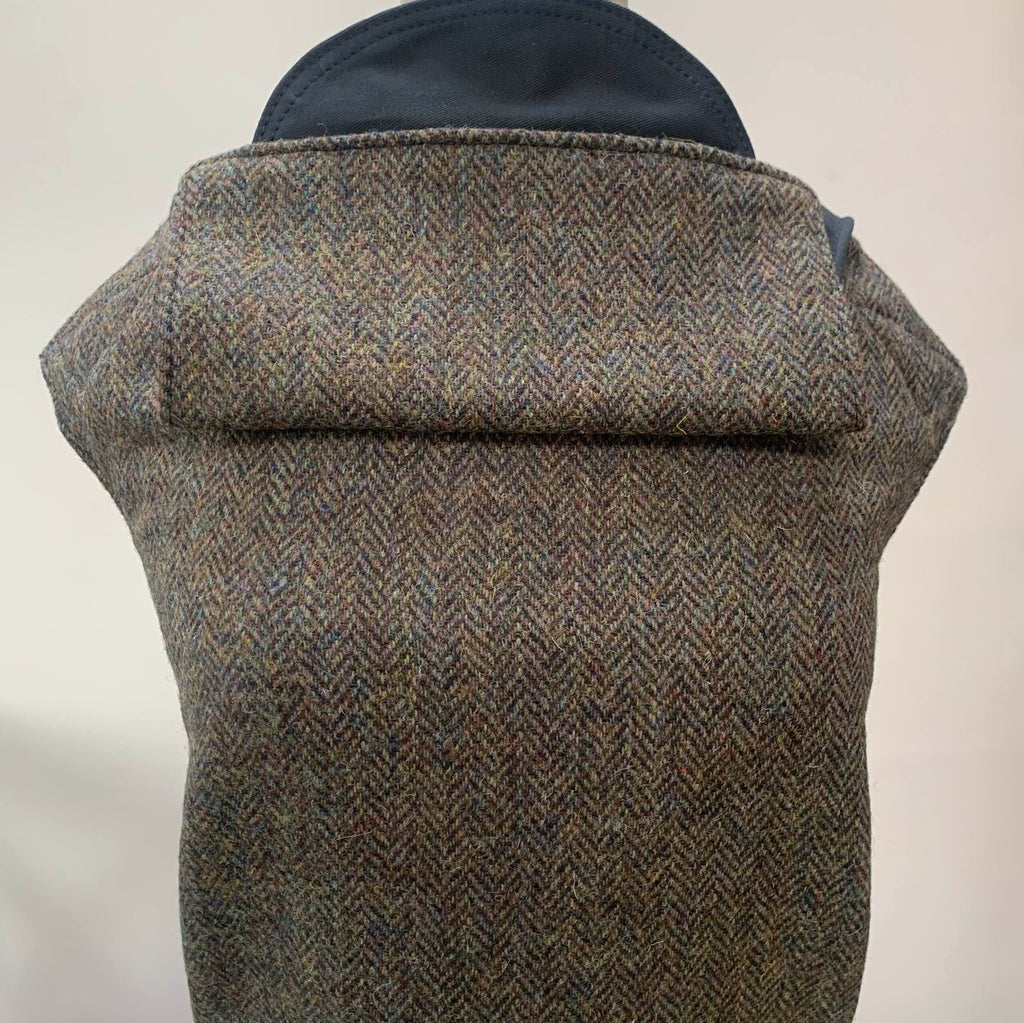 A brown Harris Tweed baby carrier with black cotton straps, showing the exterior pattern and the brand's logo.