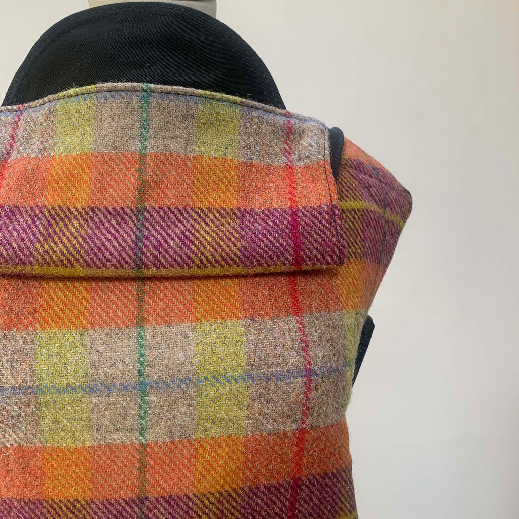 Close-up of a Harris Tweed baby carrier featuring a checkered pattern with colors including orange, green, purple, and yellow.