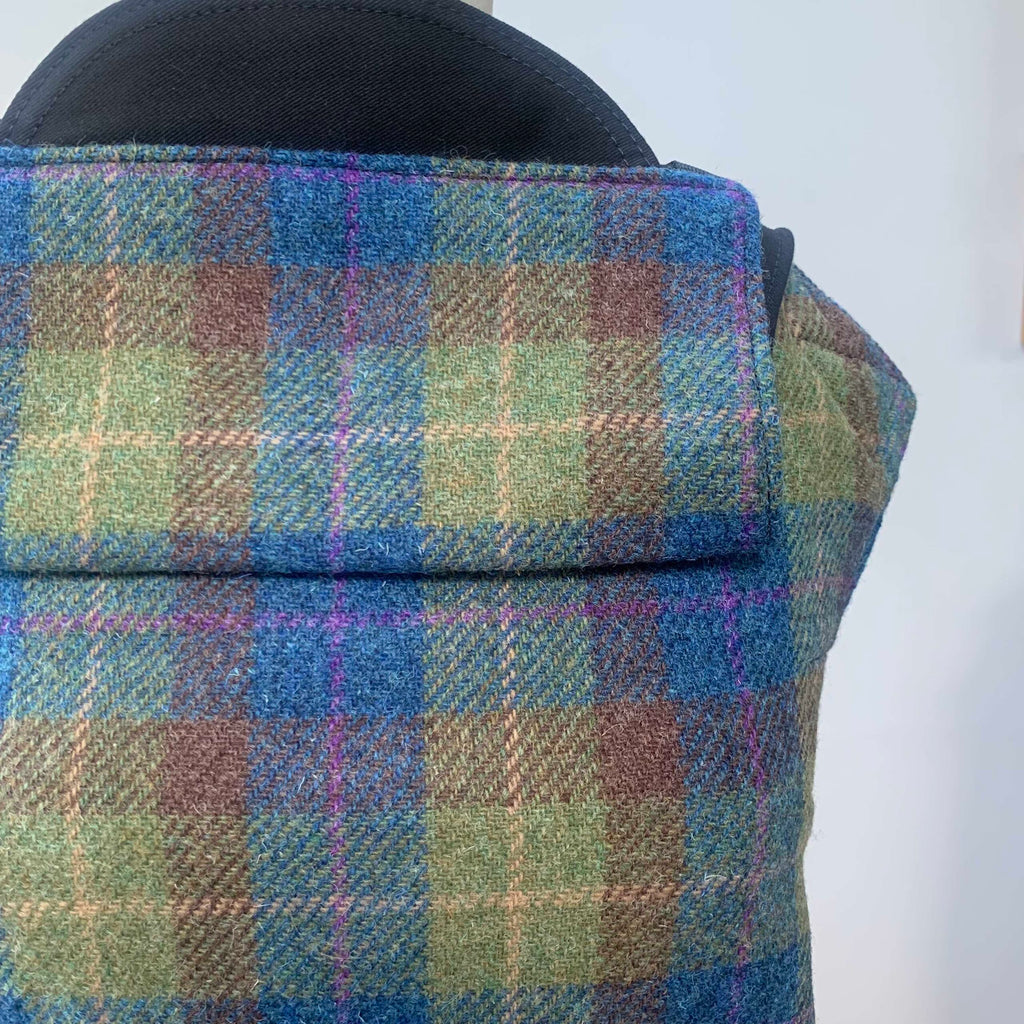 A baby carrier size 1 with Harris Tweed fabric in a plaid pattern, featuring green, blue, and brown colors, and black cotton straps.
